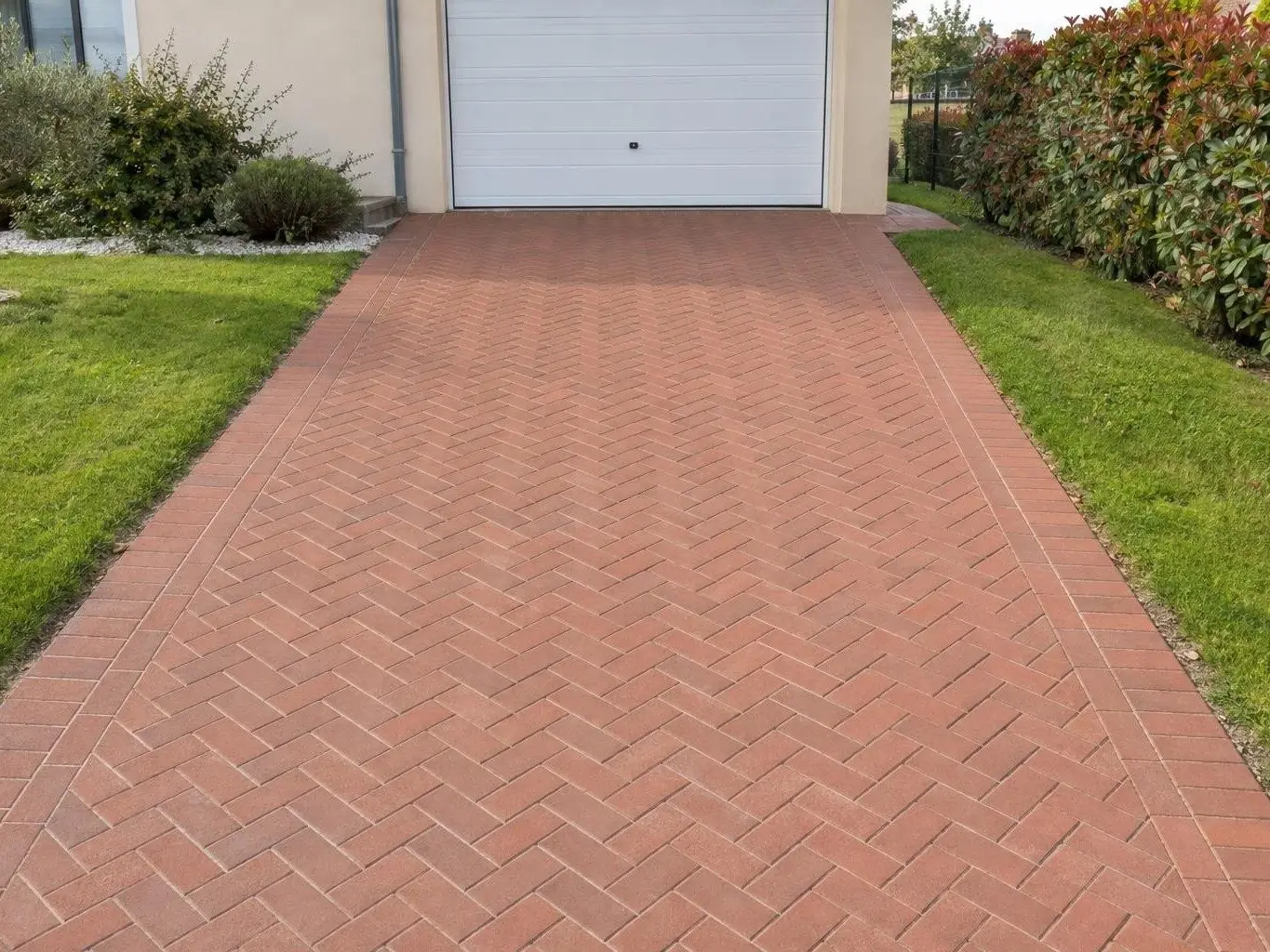 La même allée de pavés ocre rouge en chevrons, couleur vive et joints nets, devant la porte de garage blanche