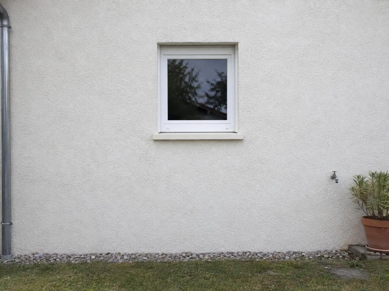 Le même mur crépi, blanc cassé, propre et uniforme autour de la petite fenêtre blanche, pot en terre cuite au pied